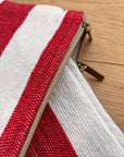 Nahaufnahme der LEY! Tasche - Stripe Line "Symia" (20x30cm), handgefertigt in Marrakesch: rot-weißes Baumwoll-Streifendesign mit zwei tanfarbenen Zippern, liegend auf Holz.