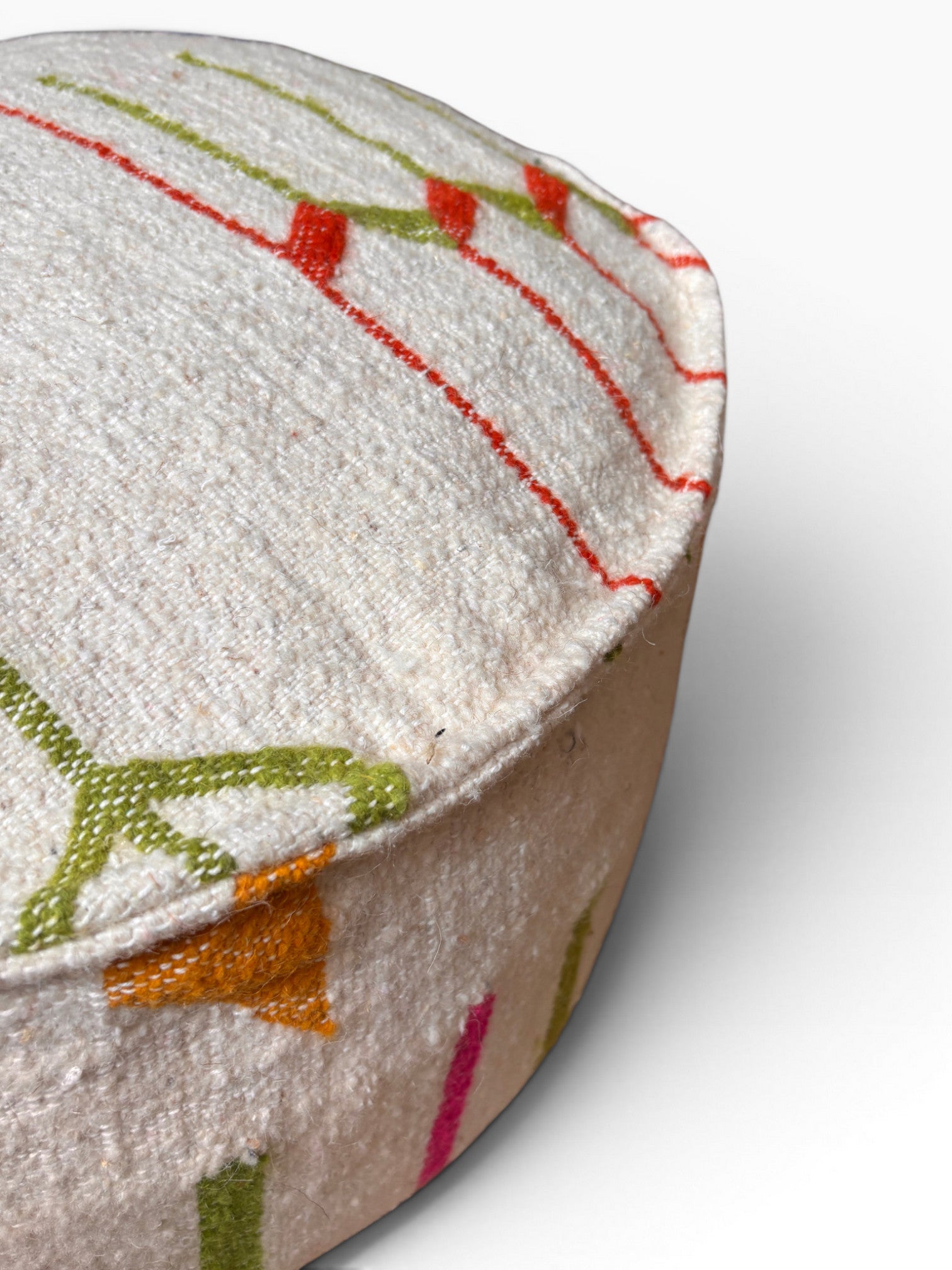 Das LEY! Bodenkissen - Colorful Line Round - Robina ist ein rundes, weißes Wollkissen mit bunten Stickmustern.