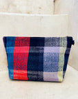 Die Tasche - Kosmetiktasche von LEY! ist handgewebt, rechteckig und hat einen Reißverschluss sowie ein buntes Karomuster in Rot, Blau, Schwarz, Gelb und Lila. Handgefertigt in Marokko und auf hellen Steinstufen platziert.