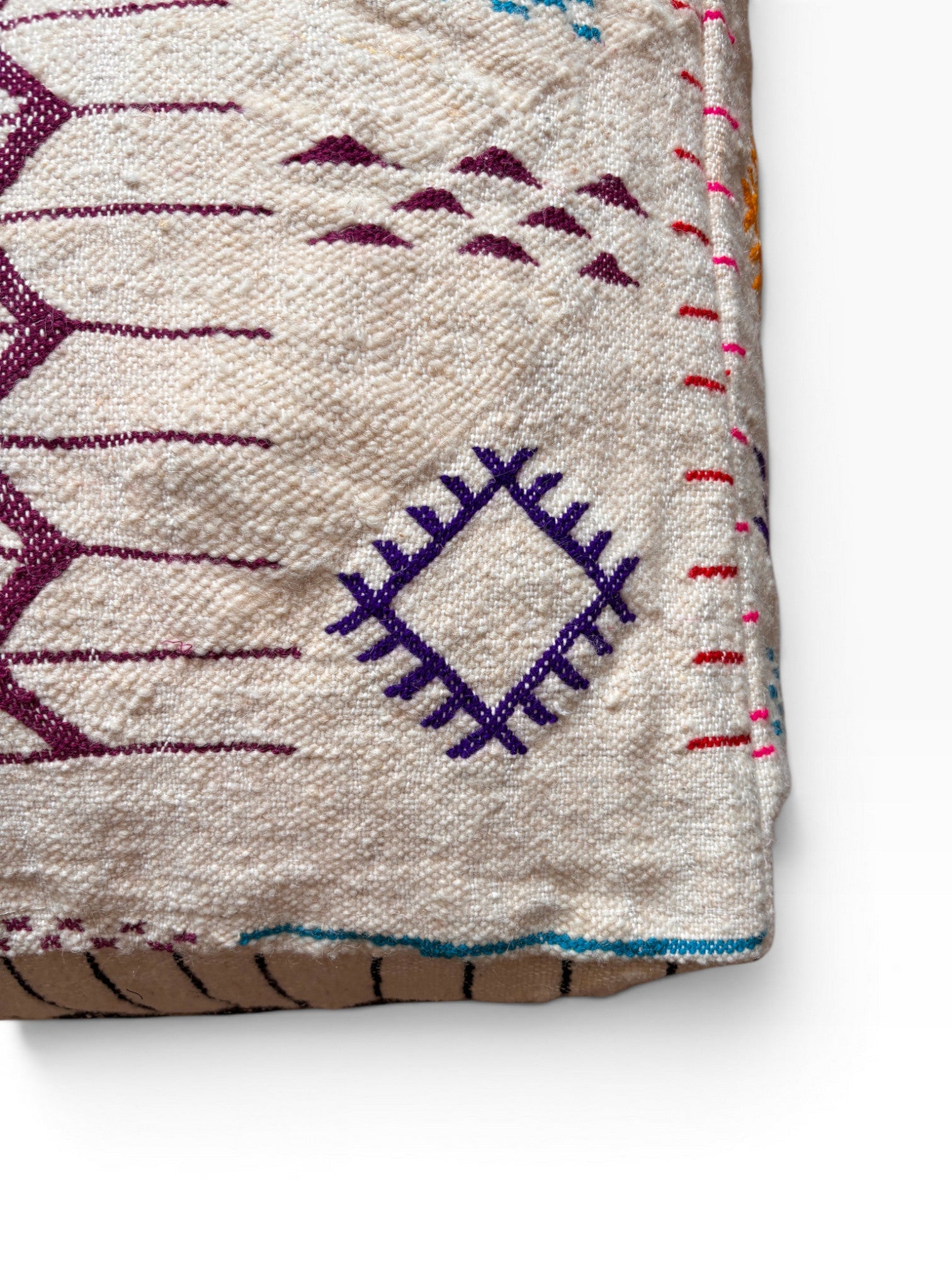 Nahaufnahme eines gewebten LEY! "Bodenkissen - Colorful Line - Limana" mit geometrischen Mustern in Lila, Blau und Rot auf Creme.