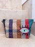 Die handgewebte Kosmetiktasche von LEY! besticht durch beige, blaue, orange und rote Streifen sowie ein gesticktes Auge in Türkis, Weiß und Pink. Das stilvolle Accessoire aus Marokko ist auf Steinstufen platziert.