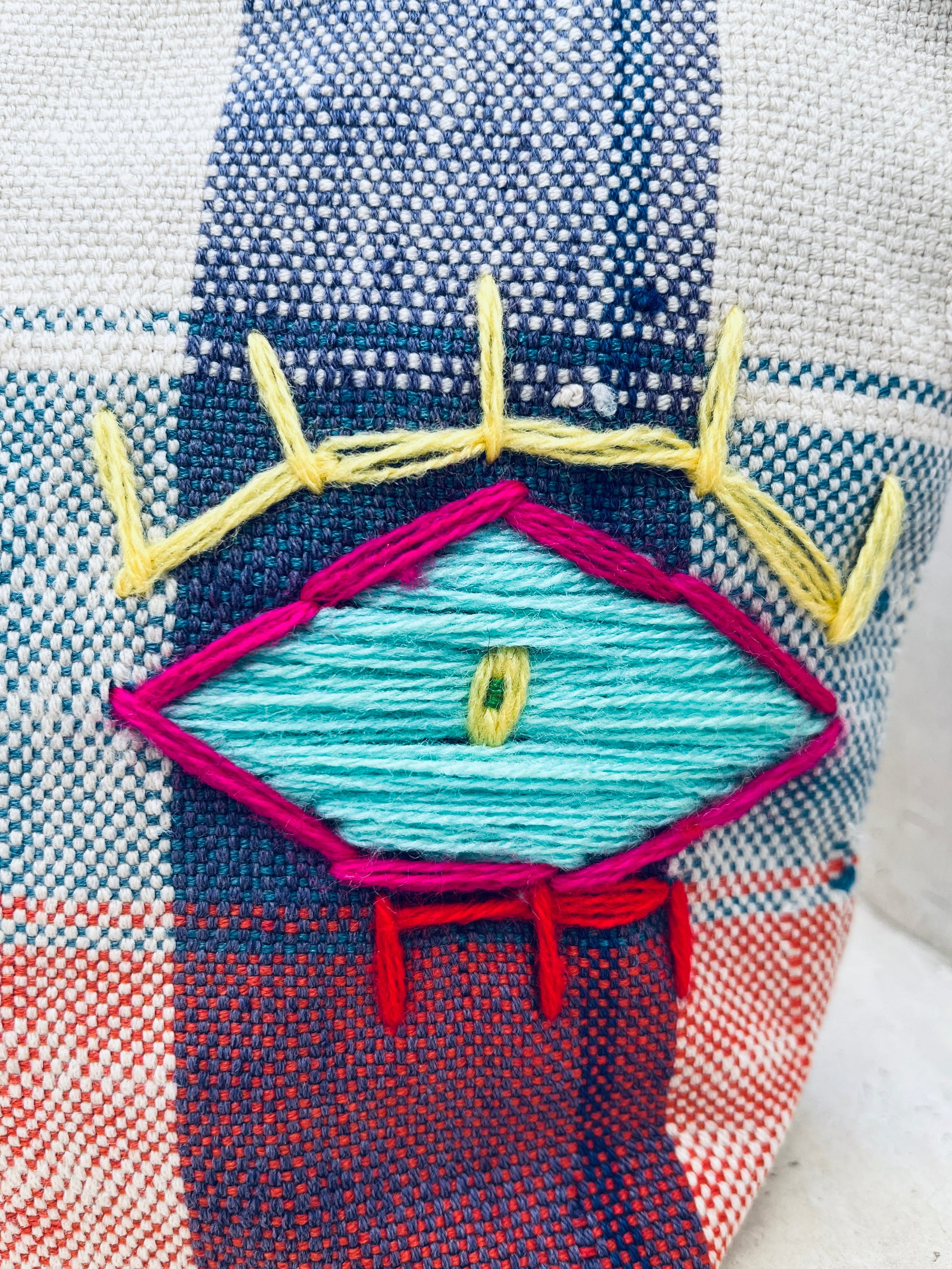 Nahaufnahme eines handgewebten Stoffes mit einem geometrischen gestickten Augenmuster in Blau, Gelb und Rosa auf einem gewebten Hintergrund in Blau, Rot und Weiß - ideal für die von Marokko inspirierte Tasche - Kosmetiktasche von LEY!.