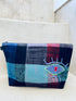 Die Kosmetiktasche "Tasche - Kosmetiktasche" von LEY! mit blau, schwarz, rot und türkis kariertem Muster sowie gesticktem Auge schmückt die hellen Betontreppen.