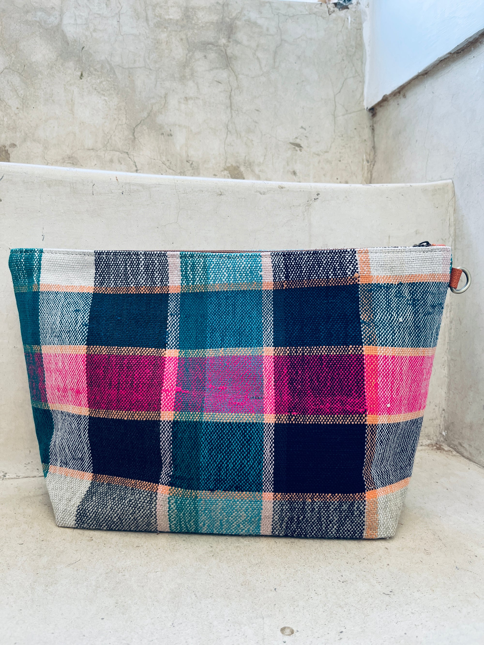 Die LEY! Tasche - Kosmetiktasche mit buntem Karomuster in Blau, Pink, Orange und Weiß liegt auf hellen Betontreppen.
