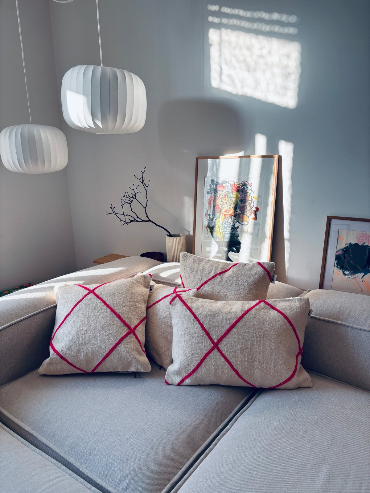 Drei beigefarbene LEY!-Kissen – Classic Line Mina 30x50 mit roten X-Motiven verleihen einem schicken grauen Sofa einen Hauch von Marrakesch.