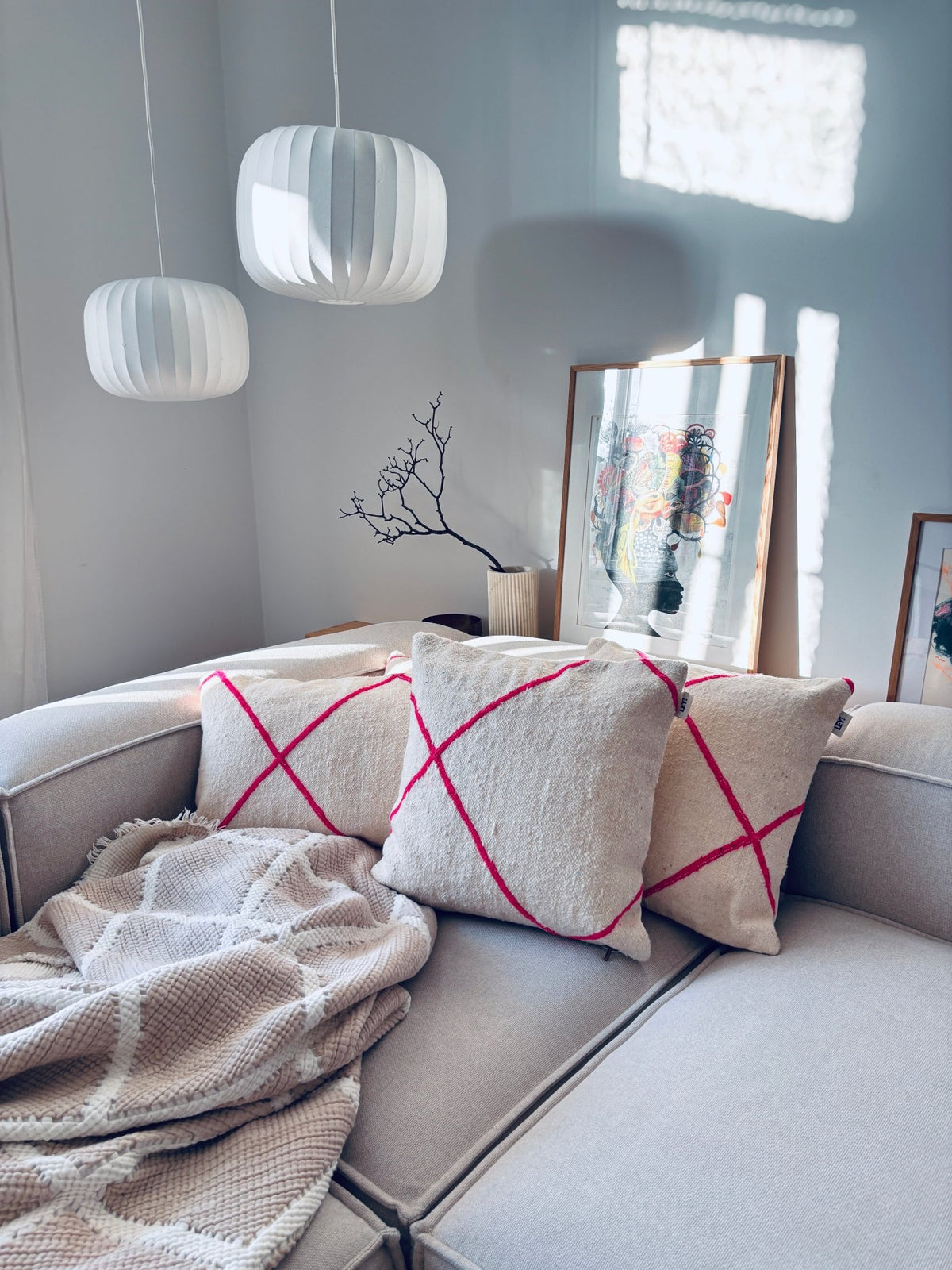 Ein gemütliches graues Sofa mit LEY!-Kissen – Classic Line Mina 30x50, einer beigen Decke und moderner Einrichtung in natürlichem Licht.