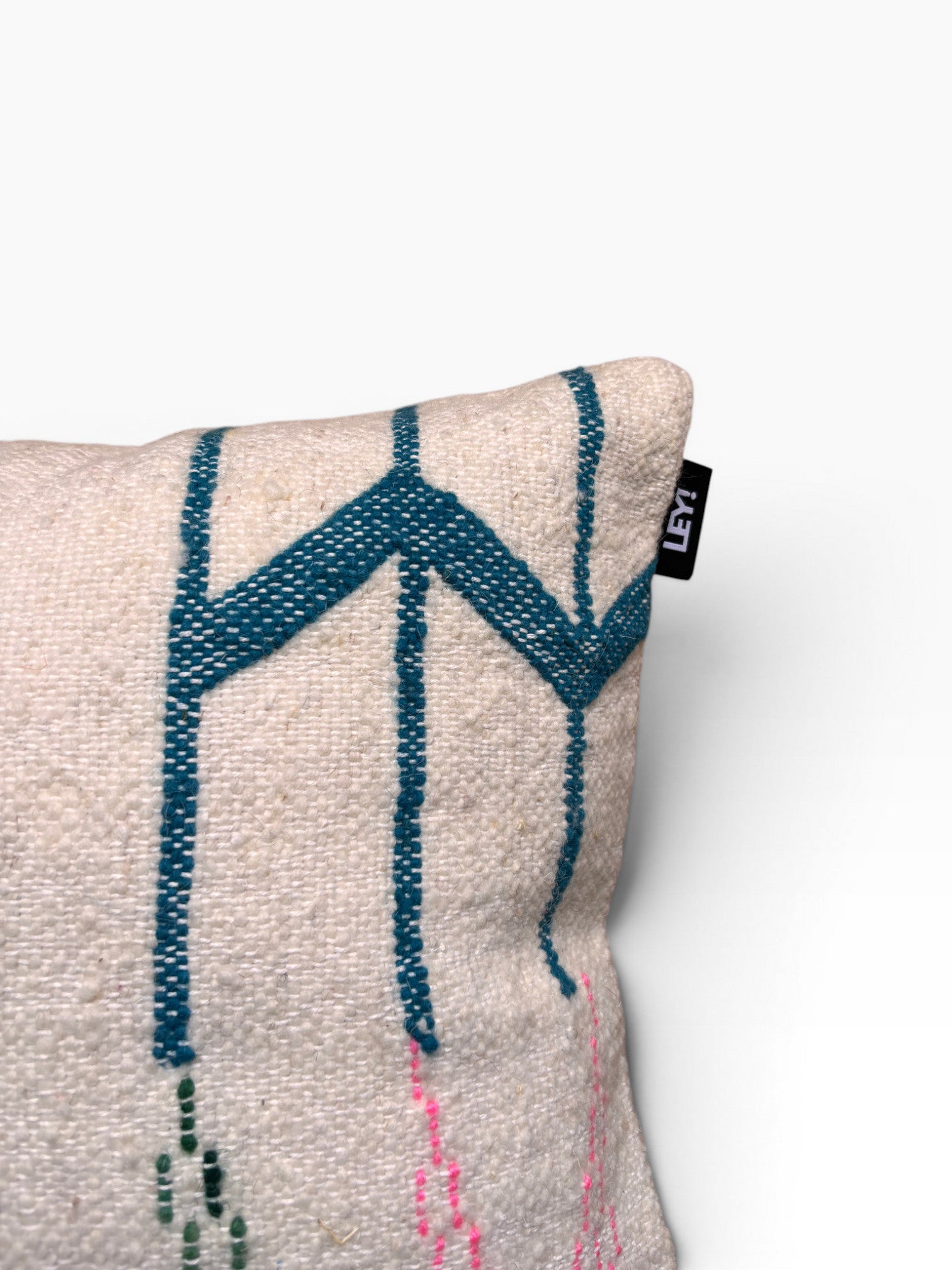 Nahaufnahme eines LEY! Kissen - Bunte Linie 40x60 mit blauen geometrischen und rosa gestickten Mustern sowie einem schwarzen "LEY!"-Anhänger.
