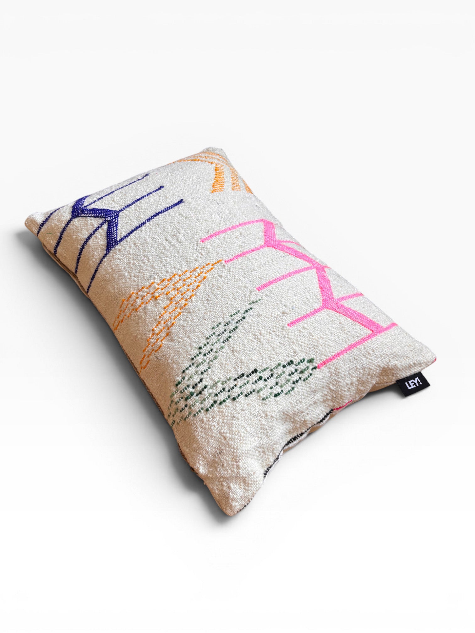 Das LEY! Kissen - Colorful Line - 40 x 60 von LEY! ist mit geometrischen Mustern und einem kleinen schwarzen Anhänger versehen.
