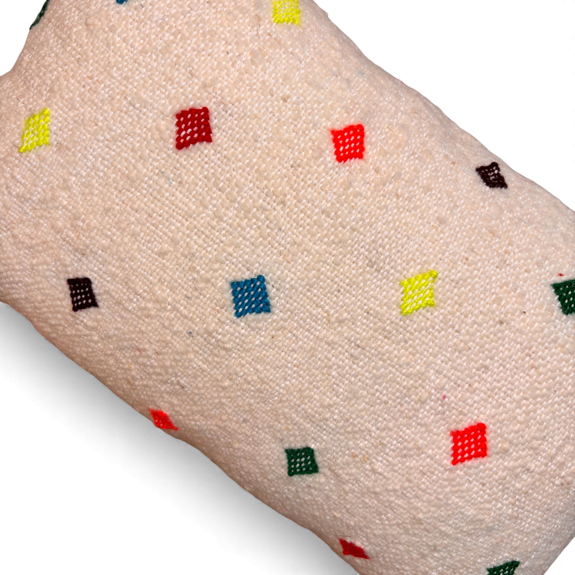 Eine Nahaufnahme zeigt das Kissen "Colorful Line - gepunktet" von LEY! (30 x 50), dessen strukturierter beigefarbener Stoff mit kleinen, bunten Punkten in Rot, Gelb, Grün, Blau und Schwarz gleichmäßig verziert ist.