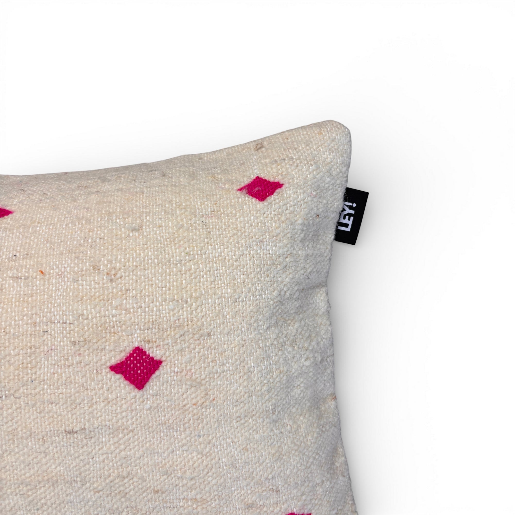 Eine Nahaufnahme des Kissens - Classic Line - Mona Pink - 40 x 60 von LEY! zeigt seine beige strukturierte Oberfläche, kleine rosa Rautenmuster und ein schwarzes LEY!-Schild auf der Naht vor einem schlichten weißen Hintergrund.