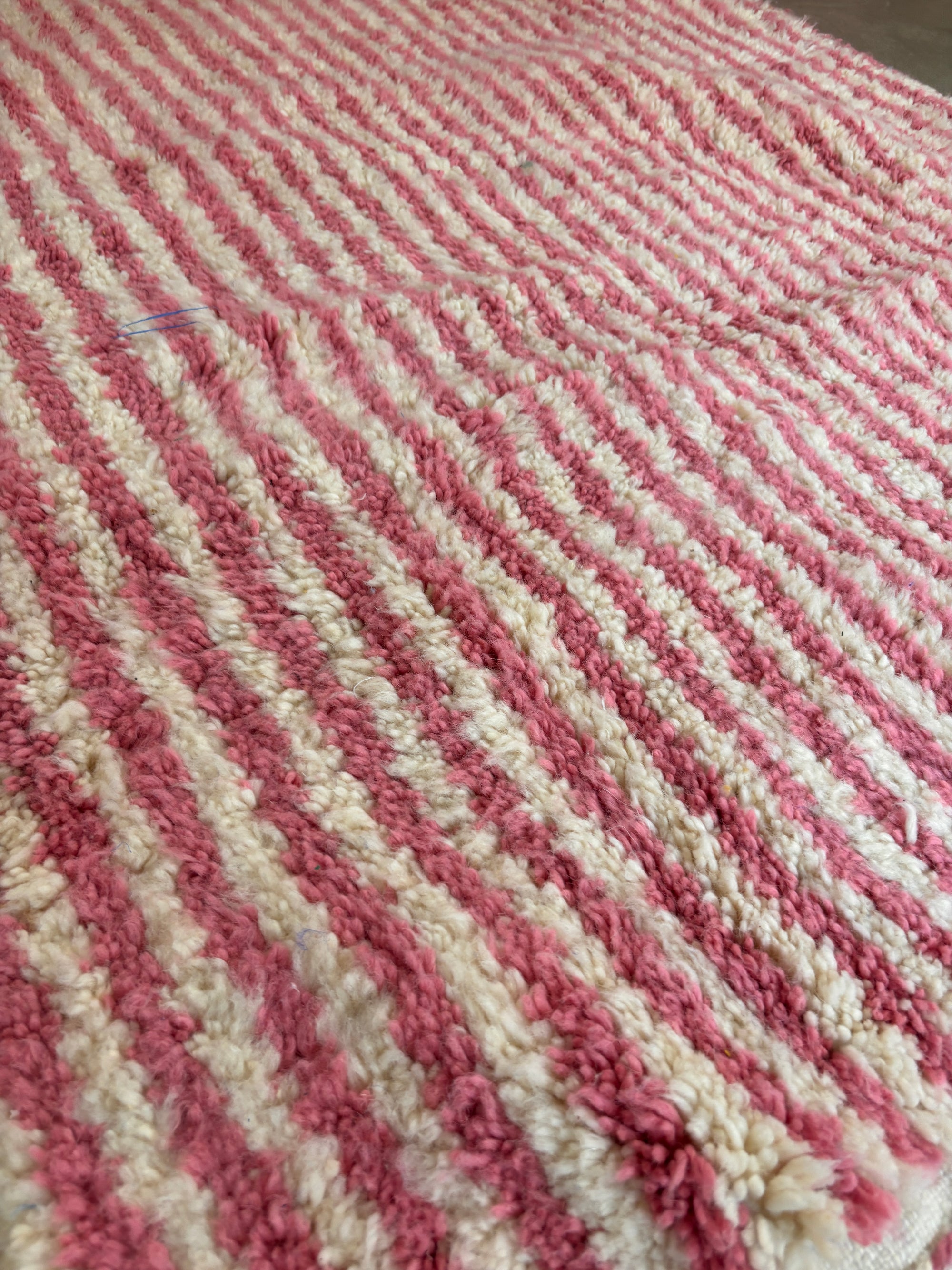 Nahaufnahme des LEY! Berber Teppich - Pinq (1,20 x 2,00), mit dicken, flauschigen Schurwolle-Fasern und abwechselnd rosa und weißen Diagonalstreifen für einen weichen Look.