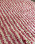 Nahaufnahme des LEY! Berber Teppich - Pinq (1,20 x 2,00), mit dicken, flauschigen Schurwolle-Fasern und abwechselnd rosa und weißen Diagonalstreifen für einen weichen Look.