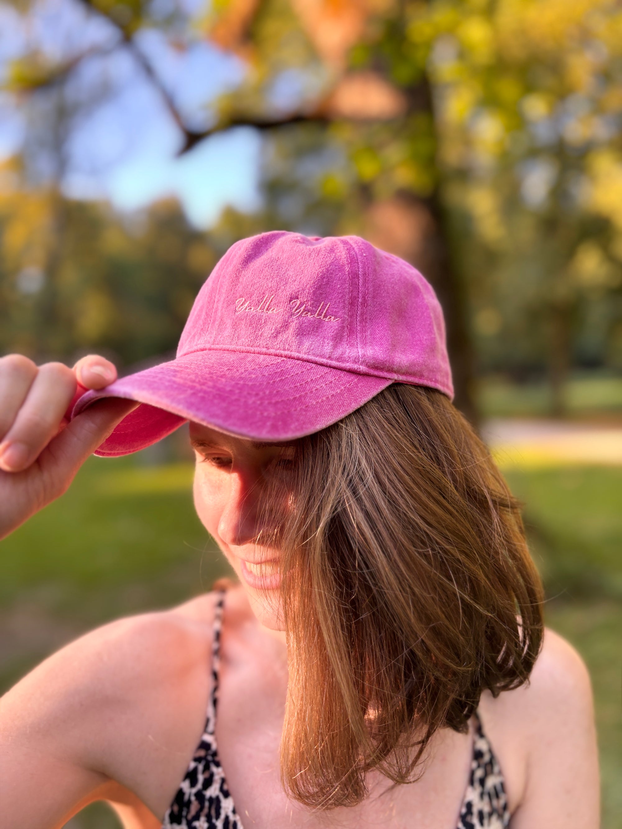 Jemand mit einer LEY!-Kappe in Lila steht draußen, hält den Schirm fest, im Hintergrund sind verschwommene Bäume zu sehen.
