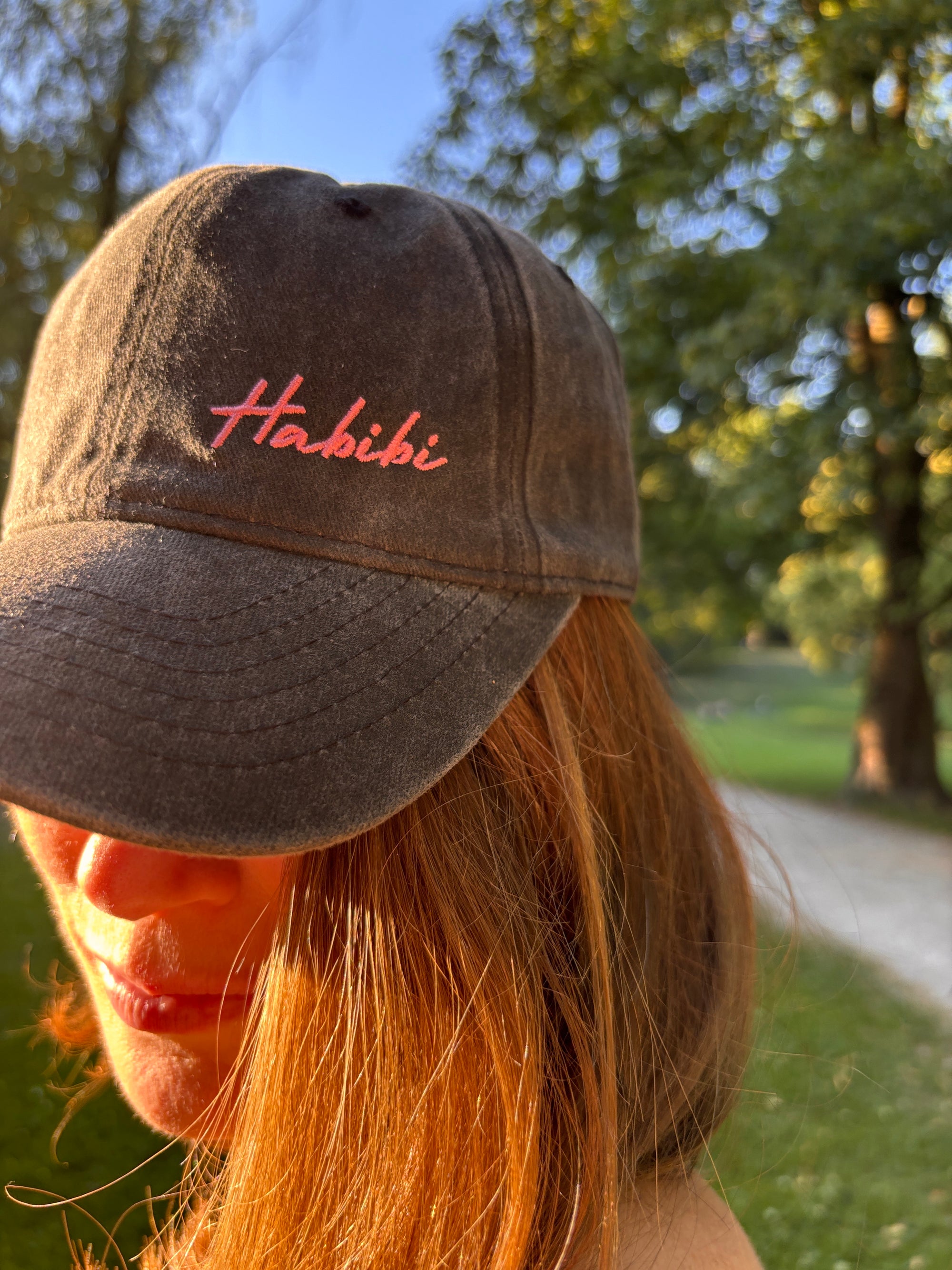 Eine Person mit langen Haaren trägt die LEY! „Habibi“-Kappe in Rosa und steht draußen im Sonnenlicht.