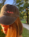 Eine Person mit langen Haaren trägt die LEY! „Habibi“-Kappe in Rosa und steht draußen im Sonnenlicht.