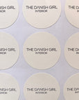 Ein runder, weißer LEY! STICKER mit "THE DANISH GIRL INTERIOR" in schwarz, angeordnet in einem Raster. Ideal als personalisierbarer Aufkleber oder Aufkleber mit Logo.