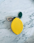 Der Schlüsselanhänger - Zitrone von LEY! ist ein kleines, gelbes, zitronenförmiges Accessoire mit grünem Blatt und Metallverschluss, ideal als Münzgeldbörse oder stilvoller Schlüsselanhänger.