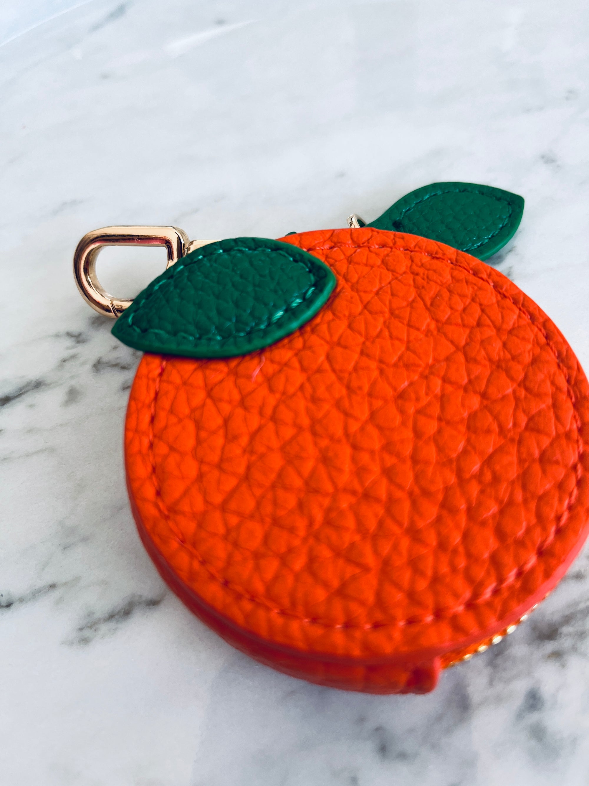 Orangefarbenes Schlüsselanhänger-Etui von LEY! mit grünen Details und Reißverschluss auf Marmortisch.