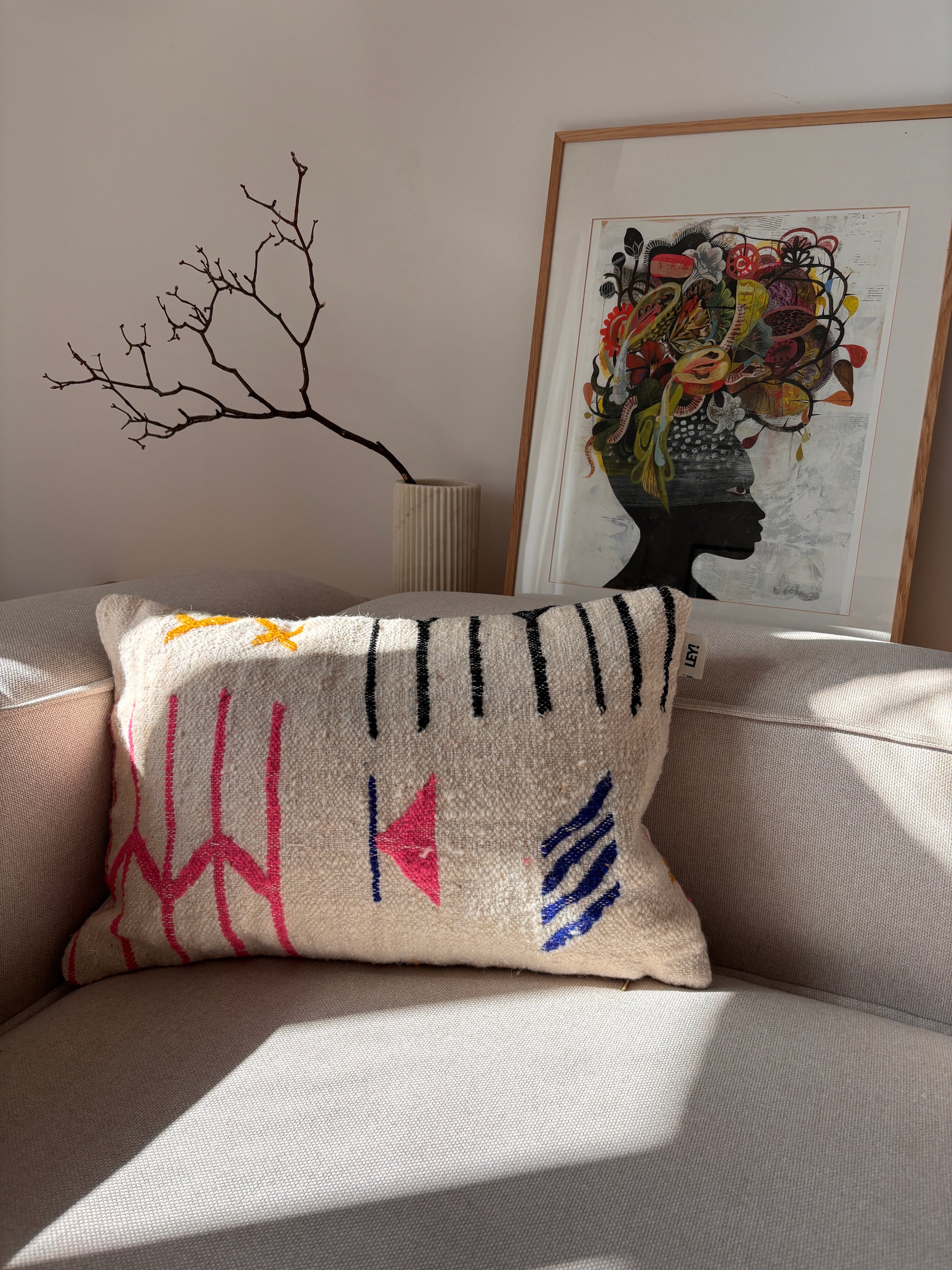 LEY! Kissen – „Colorful Line“, 40 x 60, auf einem beigen Sofa mit einer Vase mit Zweigen und einer Silhouettengrafik im Hintergrund.