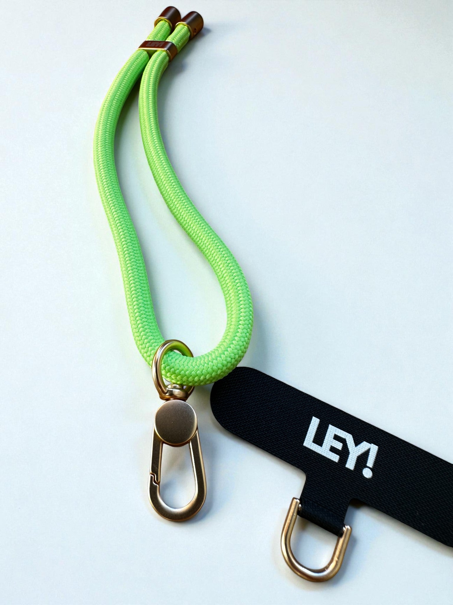 Eine neongrüne Hundeleine aus Seil mit Messingbeschlägen liegt neben einem schwarzen LEY! Schlüsselanhänger mit weißem Etikett und D-Ring aus Messing - perfekt, um Ihre Schlüssel oder Ihr Telefon griffbereit zu halten.