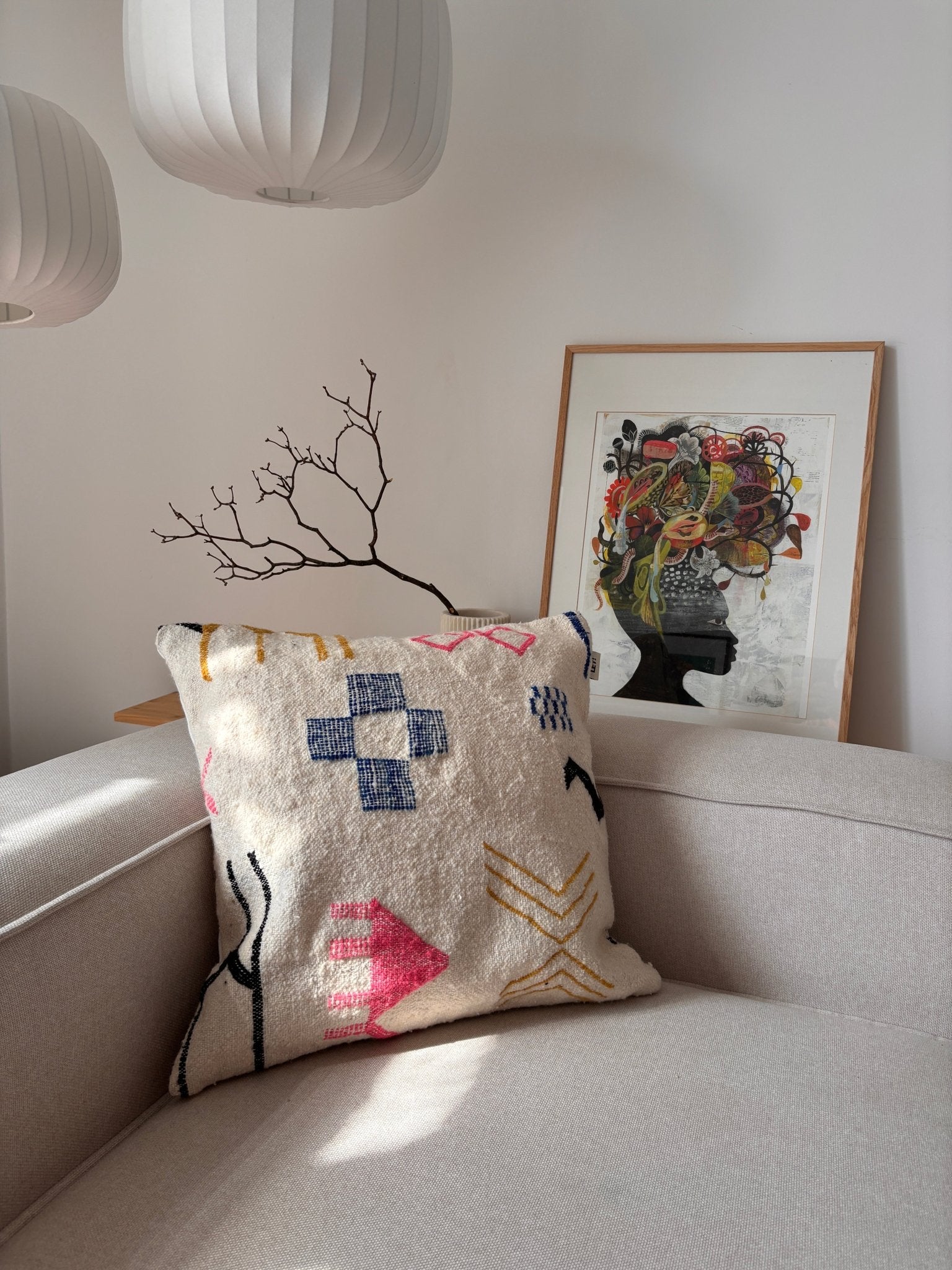 Ein LEY!-Kissen – „Colorful Line“, 60 x 60, auf einem beigen Sofa, kombiniert mit Kunstwerken und Lampen in einem hellen, stilvollen Raum.