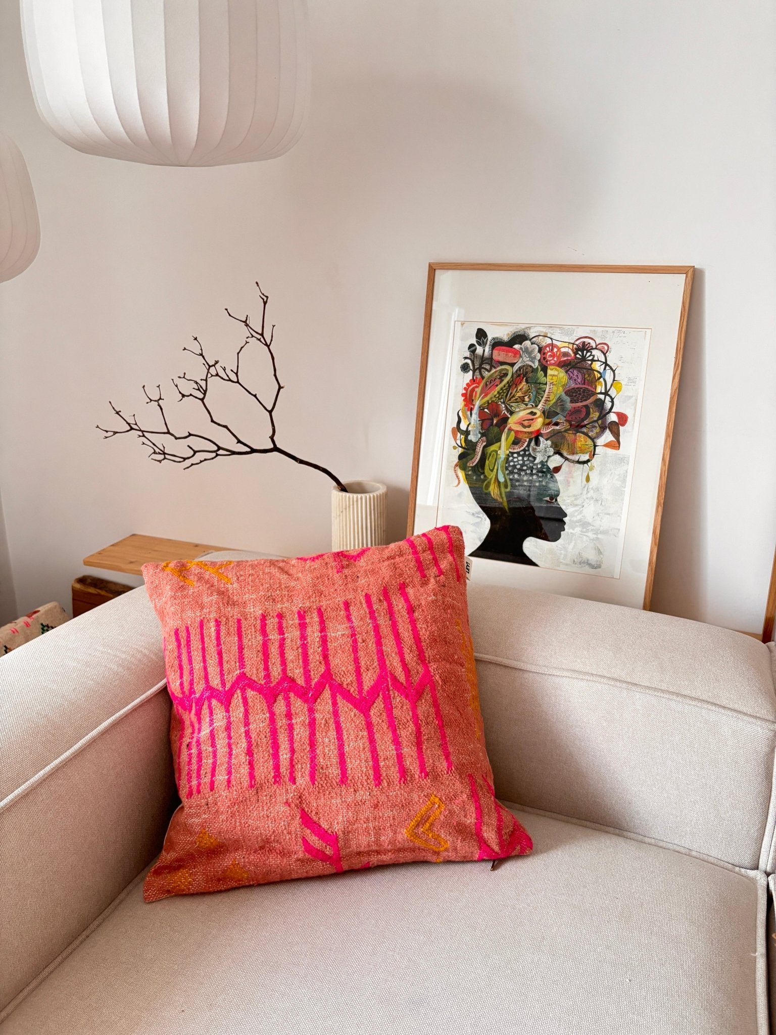 Das „A LEY!“-Kissen – Colorful Line – Terracotta Edition verleiht einem beigen Sofa mit abstrakten Motiven und einem kahlen Ast einen modernen Touch.