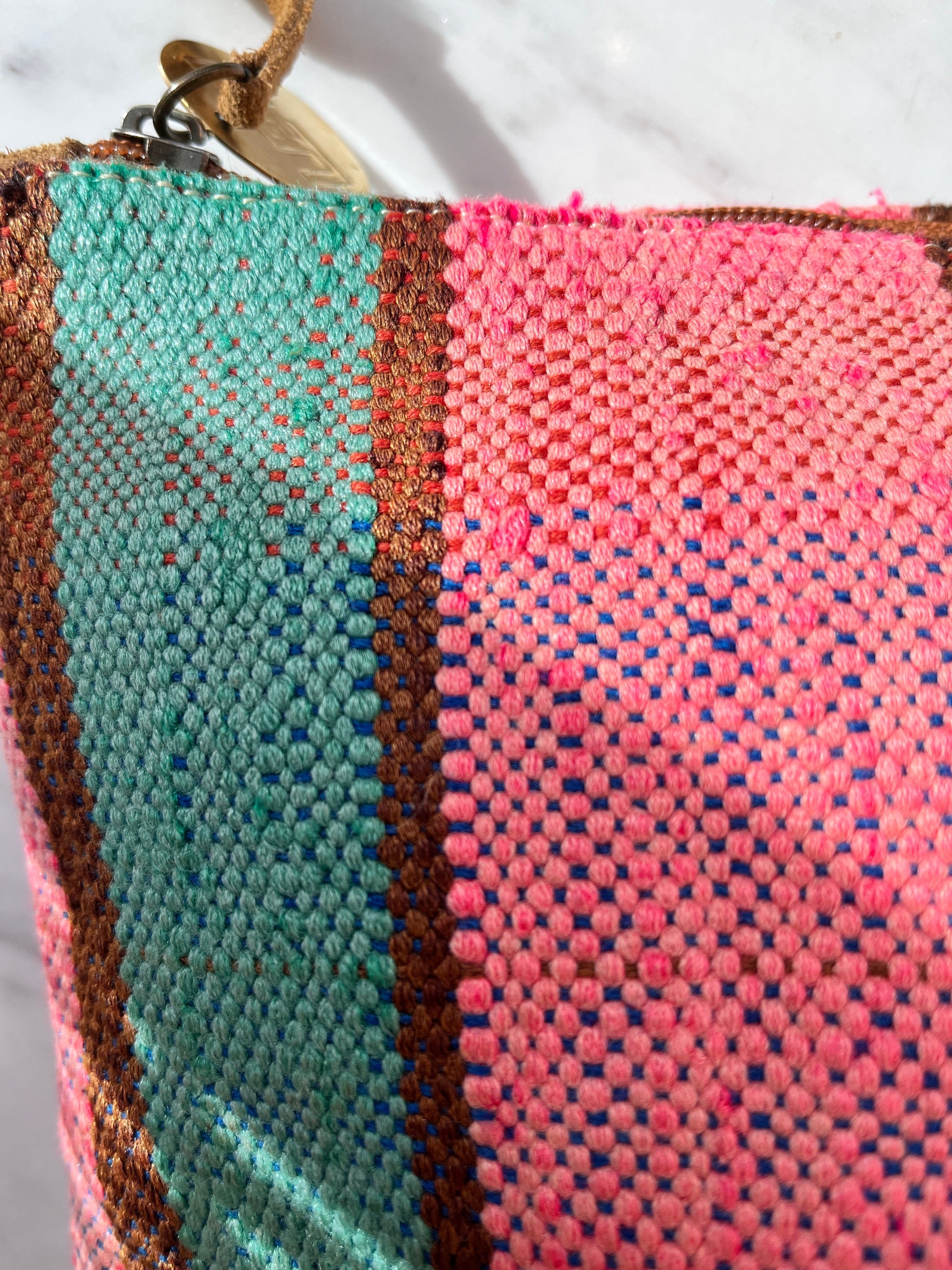 Nahaufnahme der TASCHE Clutch von LEY! - ein einzigartiges Stück aus gewebtem Stoff mit vertikalen Streifen in leuchtendem Pink, Petrol, Blau und Braun und einem hellbraunen Reißverschluss in der oberen linken Ecke.