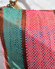 Nahaufnahme der TASCHE Clutch von LEY! - ein einzigartiges Stück aus gewebtem Stoff mit vertikalen Streifen in leuchtendem Pink, Petrol, Blau und Braun und einem hellbraunen Reißverschluss in der oberen linken Ecke.