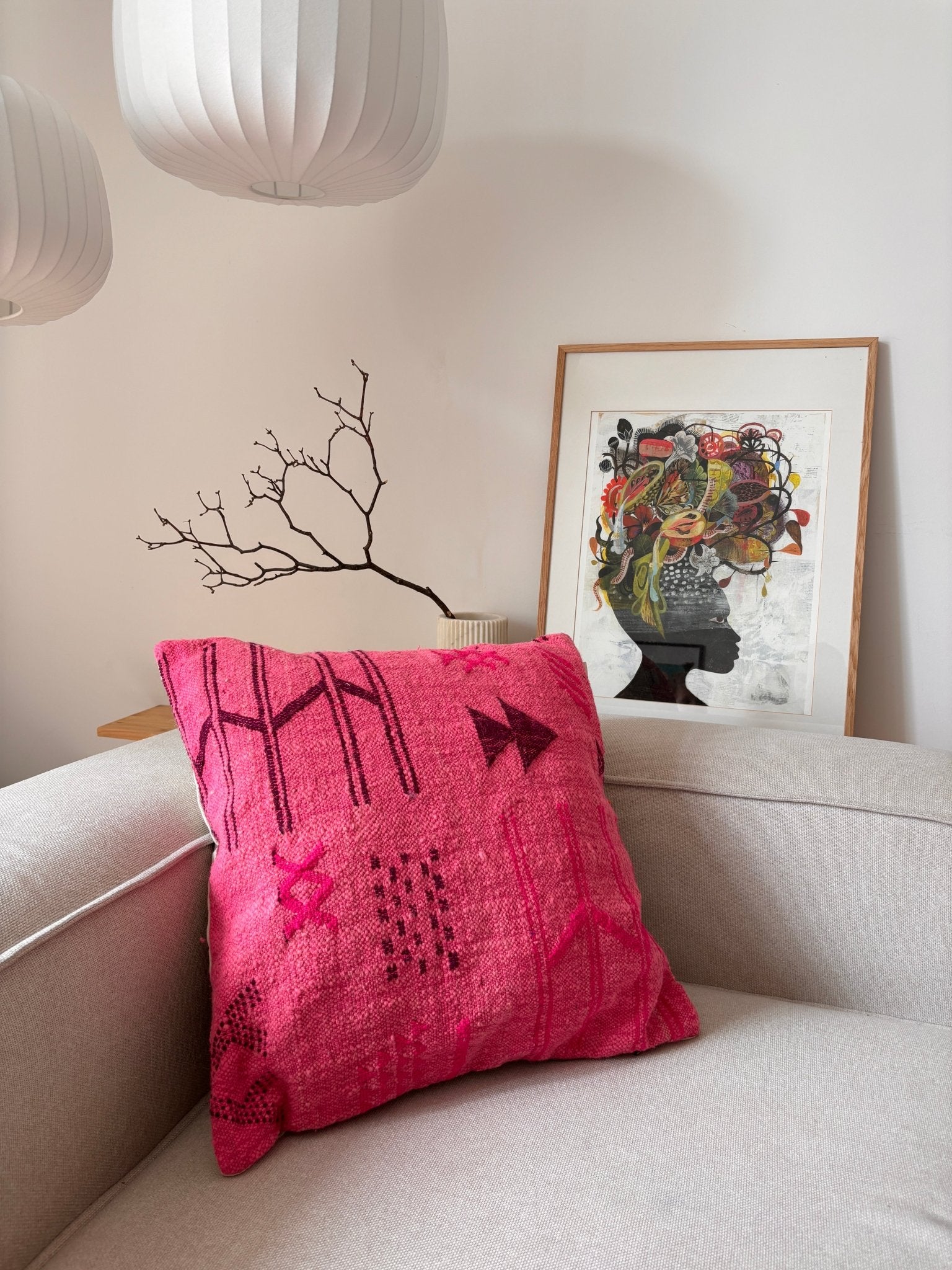 Ein LEY!-Kissen – Colorful Line – Pink Edition 50x50 liegt auf einem beigen Sofa, dahinter sind Bilder und Lampen zu sehen.