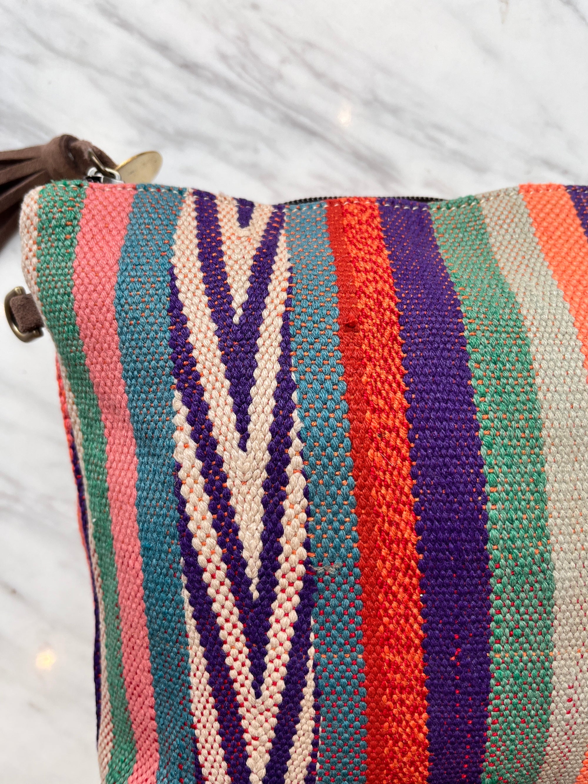 Nahaufnahme von LEY! TASCHE, einer farbenfrohen Clutch aus gewebtem Stoff mit vertikalen Streifen in Petrol, Pink, Rot, Orange, Lila und Creme. Mit Chevron-Muster und braunem Reißverschluss.