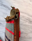 Nahaufnahme der TASCHE by LEY! - eine einzigartige, handgenähte Tasche mit roten und blauen Streifen, Lederakzenten, brauner Wildlederquaste und einem Messing-Reißverschluss mit eingraviertem Markennamen - auf einer weiß marmorierten Oberfläche.