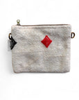 Die LEY! Tasche - Colorful Line - 15x20cm ist eine kleine beigefarbene Schurwolle-Tasche mit strukturierter Oberfläche, Reißverschluss, rotem Rauten- und schwarzem Spaten-Muster, Metallringen auf jeder Seite, weißem linken Anhänger und Teil der Colorful Line Kollektion.