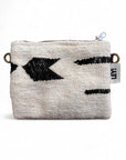 Die Tasche - Classic Line - 15x20cm von LEY! ist eine kleine, strukturierte, cremefarbene Stofftasche mit schwarzem, geometrischem Muster, einem Reißverschluss, Messingringen auf jeder Seite und einem weißen LEY!-Anhänger.