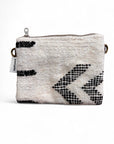 Die LEY! Tasche - Classic Line - 15x20cm ist eine kleine rechteckige Tasche mit weißem, strukturiertem Stoff und schwarzen, geometrischen Pfeilen, einem Reißverschluss an der Oberseite, seitlichen Metallringen und einem linken Stoffanhänger. Liebevoll handgefertigt in Marrakesch.