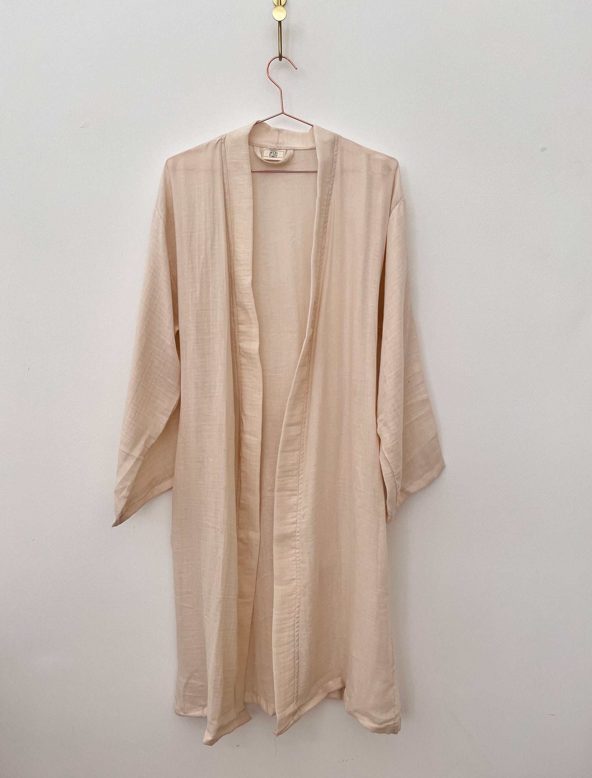 Der KIMONO - nude von BIRLIK aus Baumwolle in Einheitsgröße mit langen Ärmeln hängt an einem pinken Bügel vor einer schlichten weißen Wand.