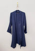 Der KIMONO - Dunkelblau von BIRLIK ist ein marineblauer, knielanger Bademantel aus Baumwolle mit langen Ärmeln und einer offenen Vorderseite. Er hat eine lockere Passform, ist in Einheitsgröße erhältlich und wird an einem goldenen Haken vor einer schlichten weißen Wand aufgehängt.
