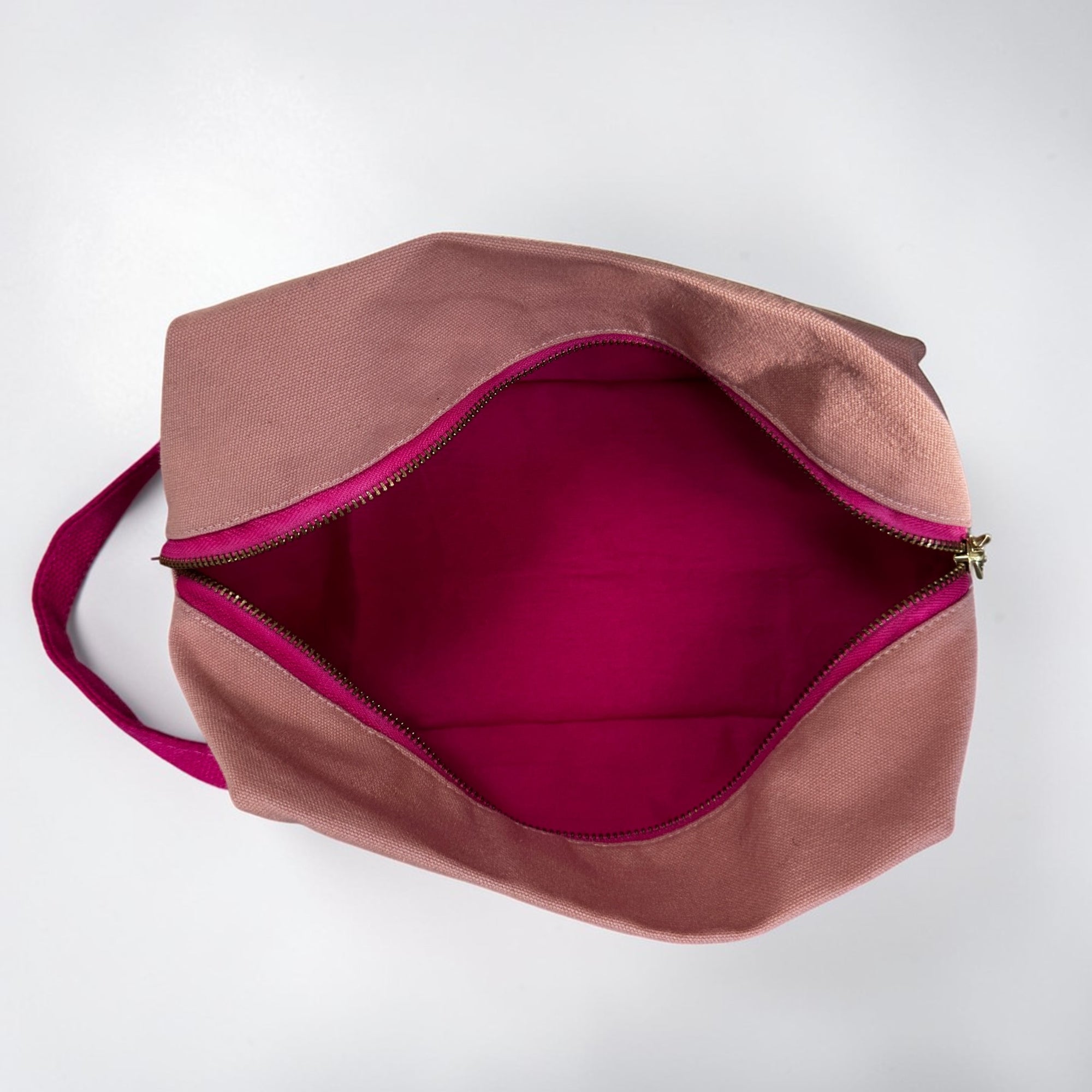 Ein Blick von oben auf die LEY! Pouch - NUDE-PINK von LEY! mit einer staubrosa Außenseite, einer hellrosa Innenseite, einem goldenen Reißverschluss und einem passenden Griff - ideal als Festival-Accessoire oder in Kombination mit anderen LEY!.