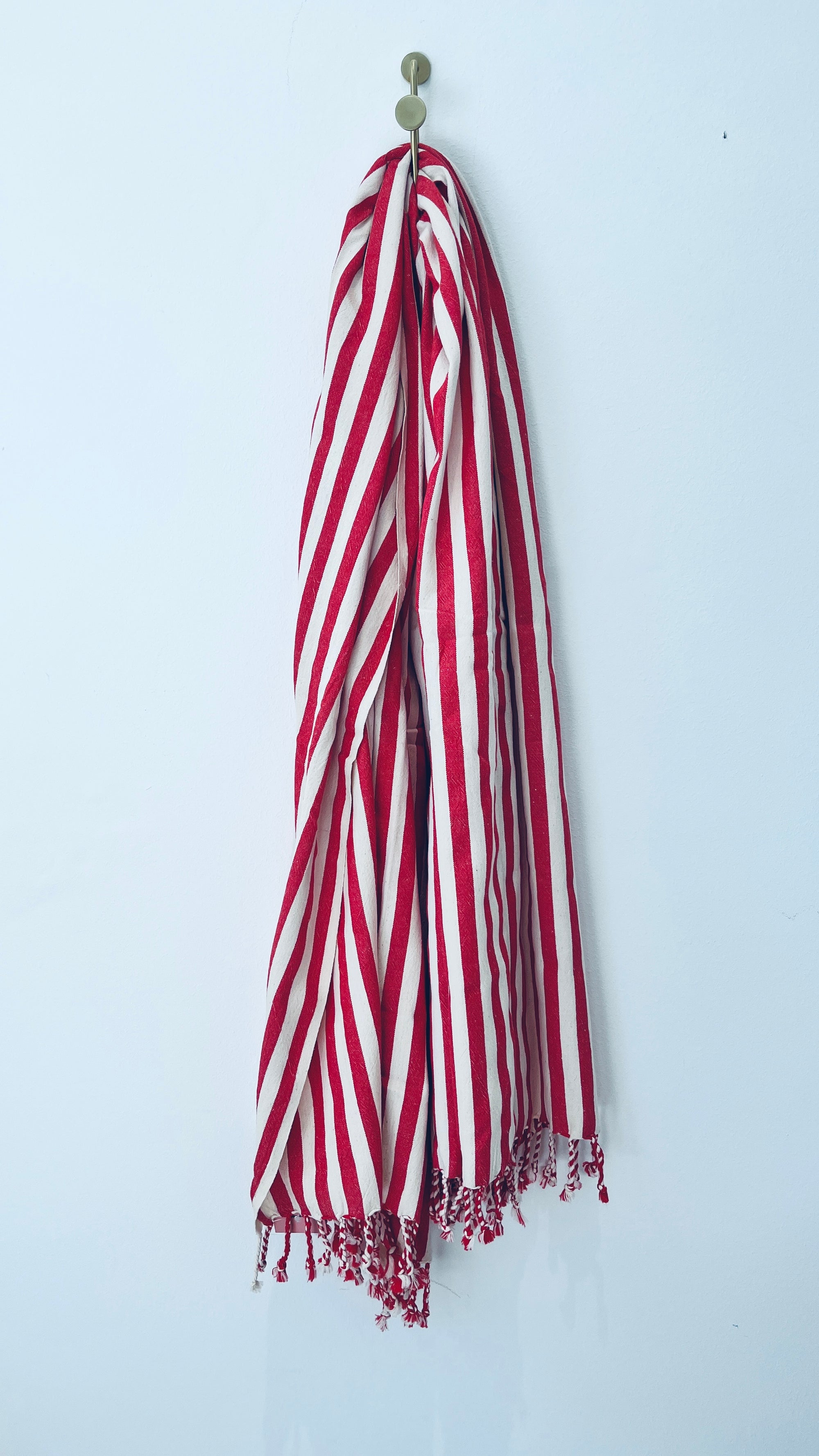Das Plaid - 90x180 rot von BIRLIK hängt ordentlich an einem goldenen Wandhaken vor einer hellblauen Wand - perfekt als leichter Überwurf oder vielseitiges Tuch für viele Anlässe.