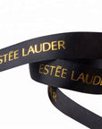 Eine Nahaufnahme eines schwarzen LEY! Bedrucktes Baumwollband mit goldenem Schriftzug, in Schleifen vor weißem Hintergrund, ideal für Premium Branding.