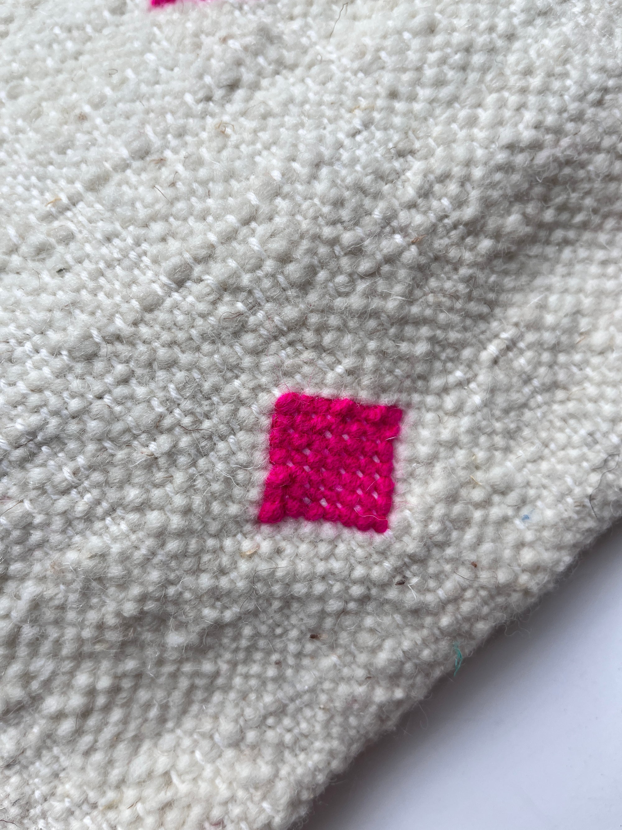 Eine Nahaufnahme der LEY! Tasche - Mona Pink (20x30cm), einer strukturierten, cremefarbenen Schurwolle-Tasche mit einem kleinen, hellrosa Quadratmuster, das in das Material gestickt ist.