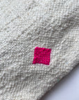 Eine Nahaufnahme der LEY! Tasche - Mona Pink (20x30cm), einer strukturierten, cremefarbenen Schurwolle-Tasche mit einem kleinen, hellrosa Quadratmuster, das in das Material gestickt ist.