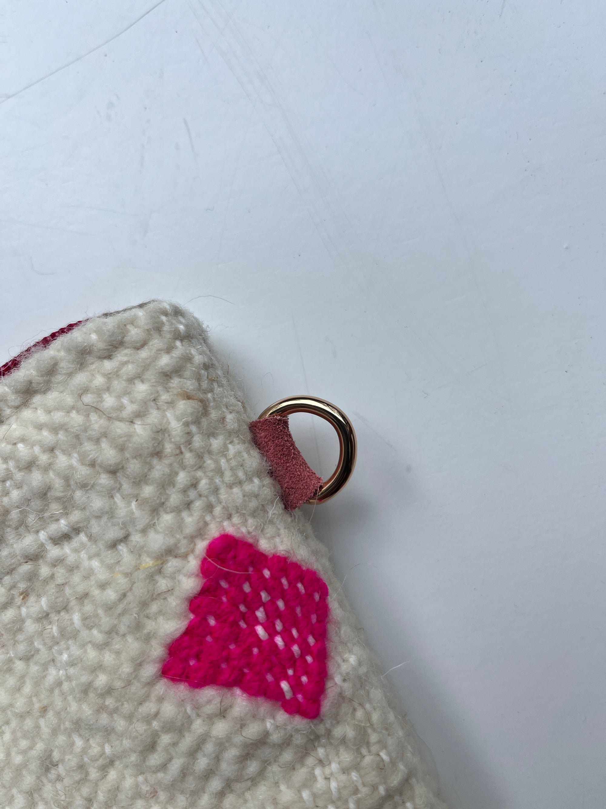 Eine Nahaufnahme der LEY! Tasche - Mona pink - 20x30cm, handgefertigt aus Marrakesch Schurwolle in creme, mit einem hellrosa genähten Quadrat und einem goldenen Metallring auf einer kleinen braunen Lasche, vor einem schlichten weißen Hintergrund.