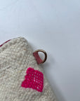 Eine Nahaufnahme der LEY! Tasche - Mona pink - 20x30cm, handgefertigt aus Marrakesch Schurwolle in creme, mit einem hellrosa genähten Quadrat und einem goldenen Metallring auf einer kleinen braunen Lasche, vor einem schlichten weißen Hintergrund.