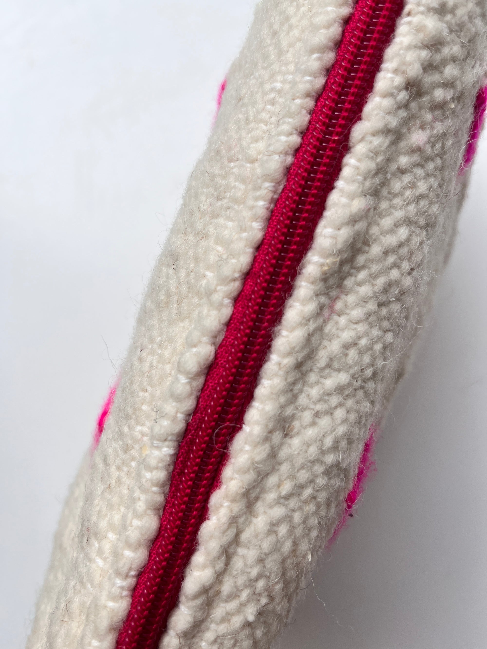 Nahaufnahme der LEY! Tasche - Mona Pink - 20x30cm: handgefertigte cremefarbene Schurwolle, ein vertikaler Reißverschluss in leuchtendem Pink, sichtbare Nähte und pinke Flecken verleihen dieser praktischen Kosmetiktasche Charakter.