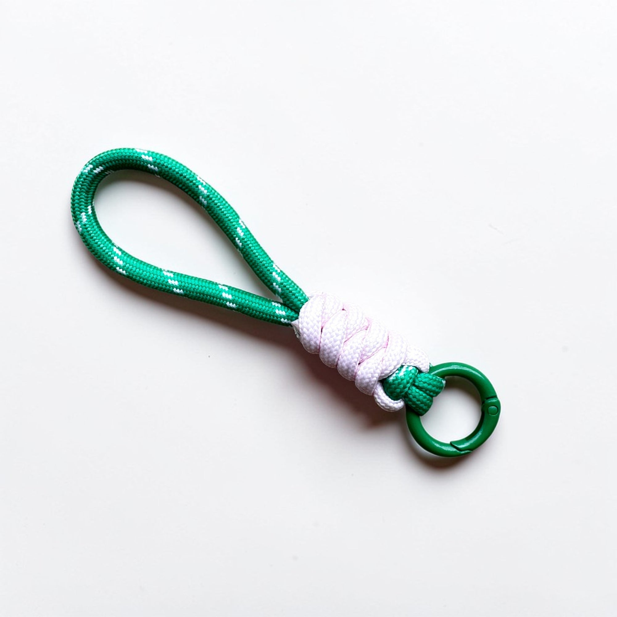 Der LEY! Schlüsselanhänger - grün - weiß - rosa besteht aus einer grünen Kordel mit weißen Akzenten und rosafarbenen Details, die durch eine weiße Umwicklung gesichert und an einem kleinen grünen Metallring befestigt ist. Er ist ein schickes Accessoire vor einem schlichten weißen Hintergrund.