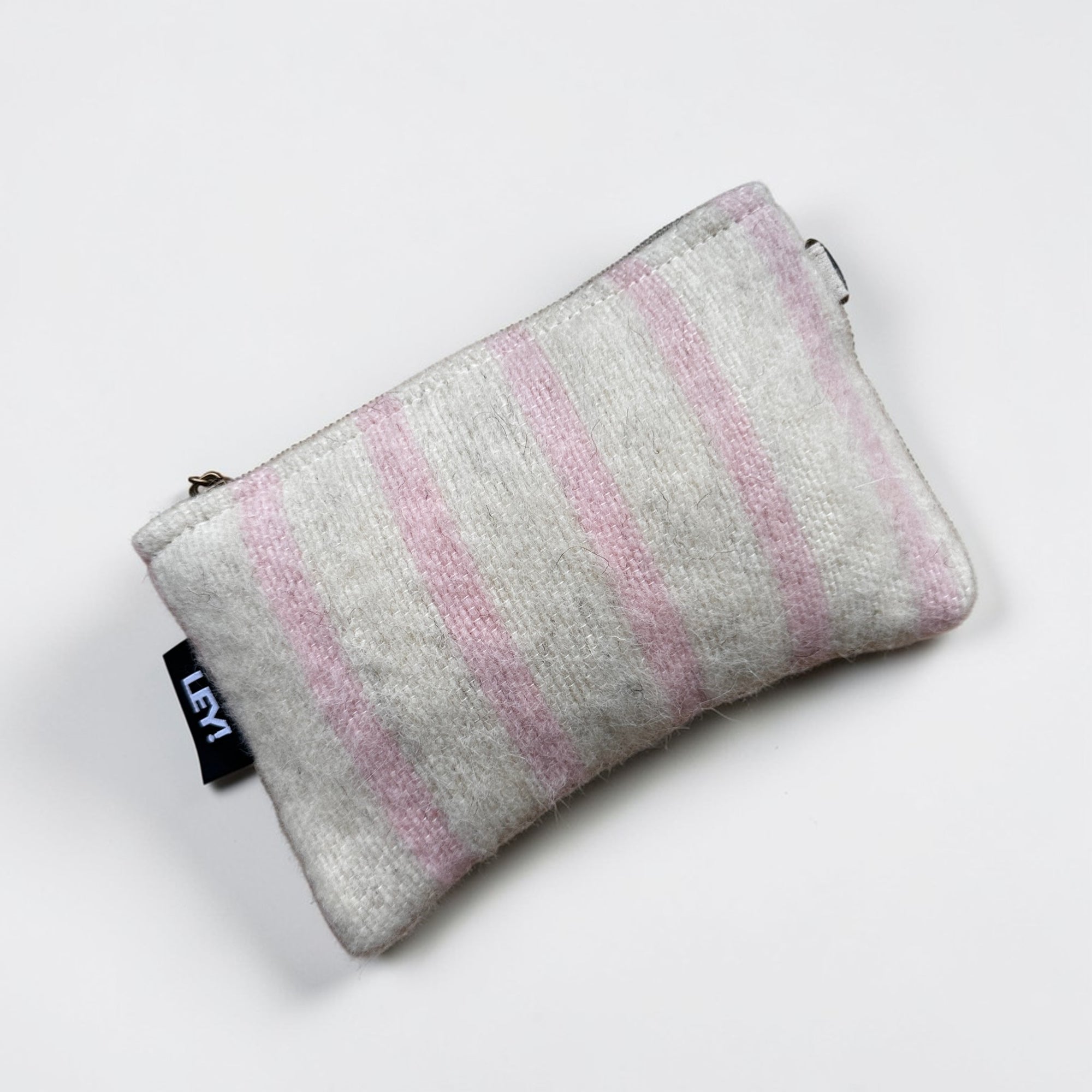 Entdecken Sie die LEY! Tasche - WINTER EDITION - PUDER (15 x 20 cm), eine handgefertigte Tasche mit Reißverschluss aus weicher Schurwolle mit hellrosa und weißen Streifen, die mit einem schwarzen Seitenanhänger versehen ist - exklusiv in Marrakesch hergestellt.