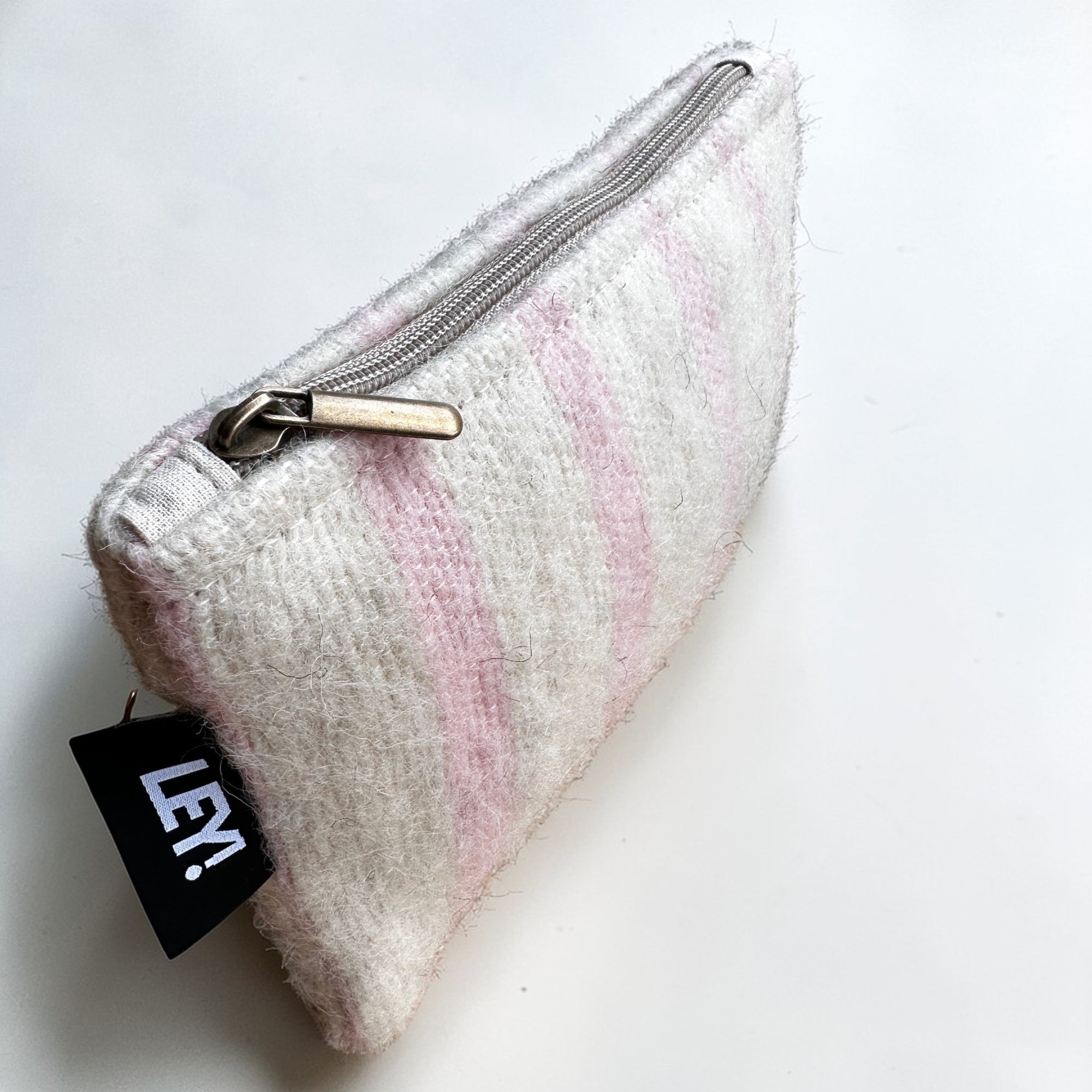Die LEY! Tasche - WINTER EDITION - PUDER (15 x 20 cm) besteht aus weicher Schurwolle mit hellrosa und weißen Streifen, einem Metallreißverschluss und einem schwarzen LEY!-Anhänger - gefertigt in Marrakesch.