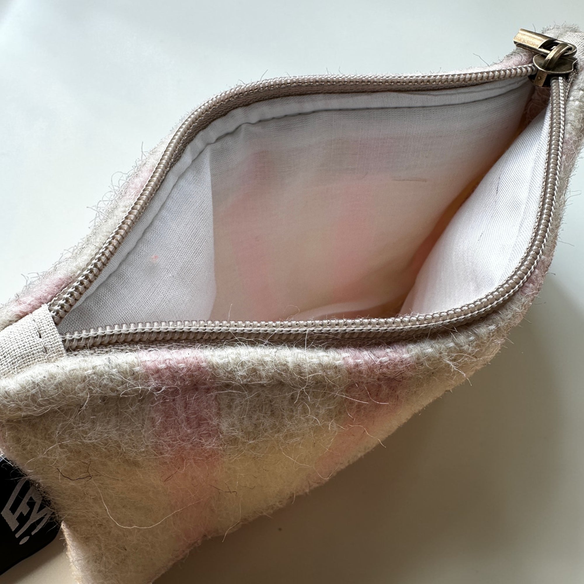 Eine Nahaufnahme einer geöffneten LEY! Tasche - WINTER EDITION - PUDER (15 x 20 cm) aus cremefarbenem Stoff mit rosafarbenen Details und weißem Innenfutter auf einer weißen Fläche.
