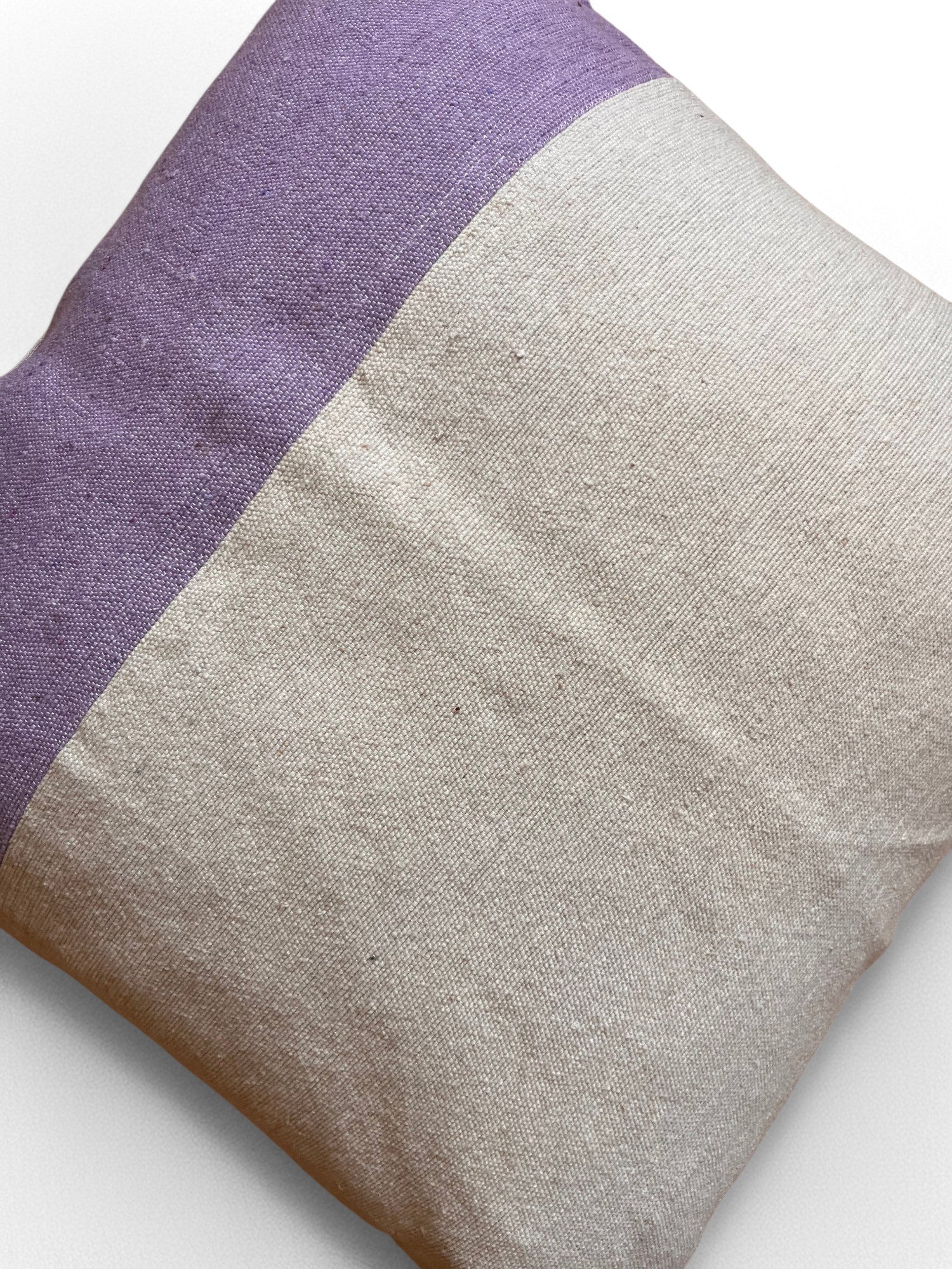 Das Kissen - Dilara 60x60 von LEY! zeigt ein handgefertigtes Marrakesch-Dessin mit hellbeigem und violettem Stoff in diagonaler Teilung, aus der LEY Spring Line, auf weißem Untergrund.