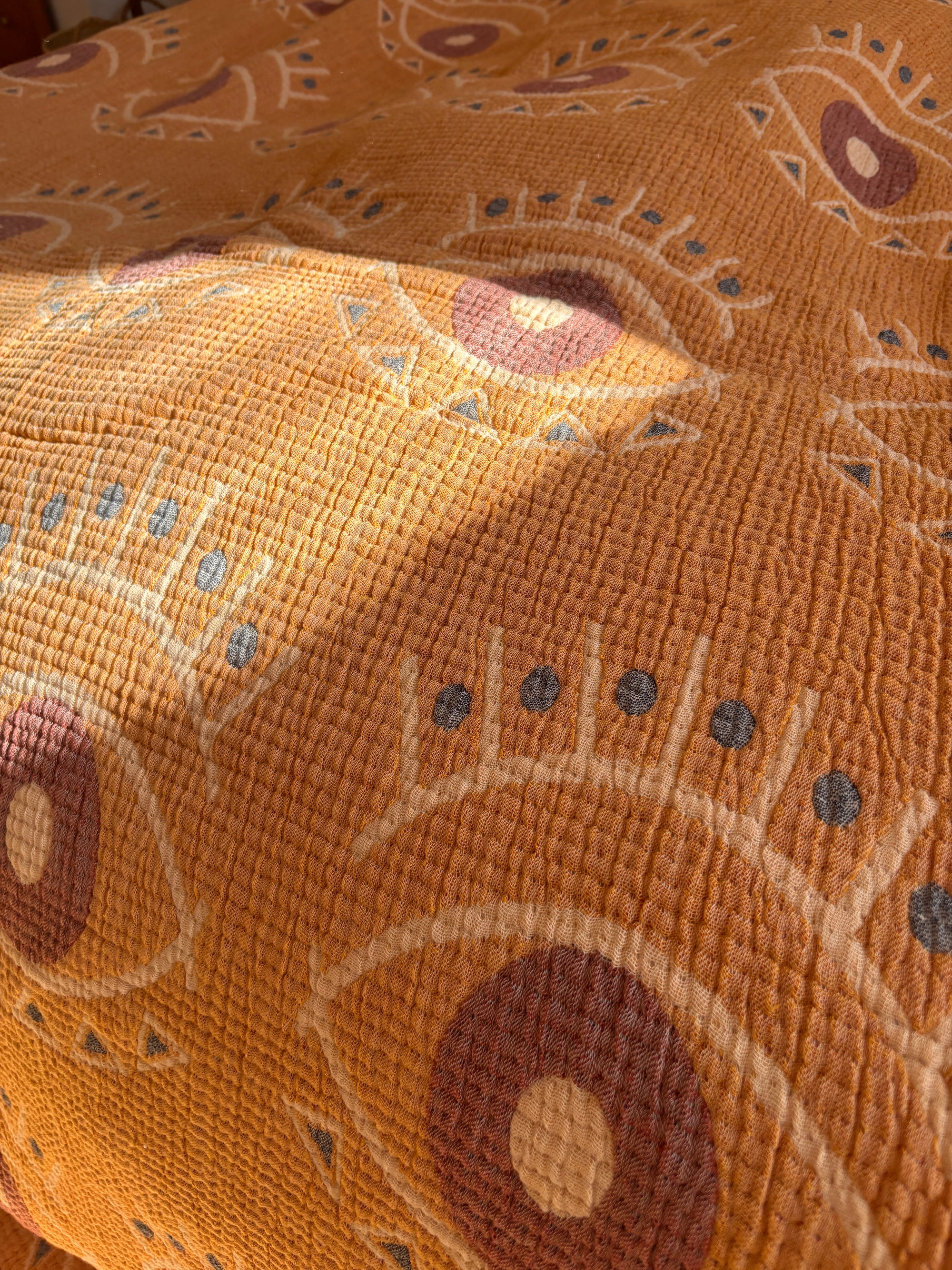 Eine Nahaufnahme der LEY! Musselin Decke - Vision in Gelb-Blau (2,20 x 2,50 m) zeigt im Sonnenlicht abstrakte Augenmuster in Beige, Braun und Grau - ideal, um Ihrem Raum ein Boho-Design-Flair zu verleihen.